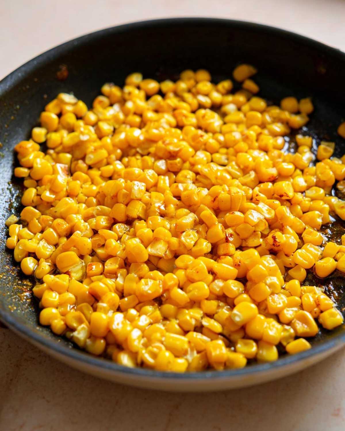 Close-up view of bright yellow corn kernels sizzling in a dark skillet, preparing Honey Butter Skillet Corn.