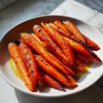 A white bowl filled with glossy, roasted Honey Garlic Butter Carrots, showing caramelized edges and butter pooling at the bottom.