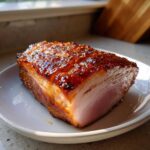 A thick slice of ham with a dark, shiny honey glaze and mustard seeds, ready for the Honey Glazed Easter Ham Recipe.