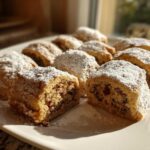 Close-up of several Italian nut roll cookies dusted heavily with powdered sugar on a white plate.