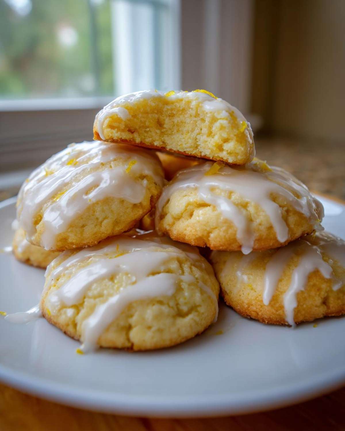 A stack of soft Italian ricotta cookies topped with thick white lemon glaze and zest.