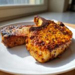 Two thick, bone-in air fryer pork chops seasoned with a rich, orange-red spice rub, resting on a white plate.
