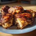 Close-up of several perfectly cooked, glazed chicken thighs with crispy skin served on a white plate.