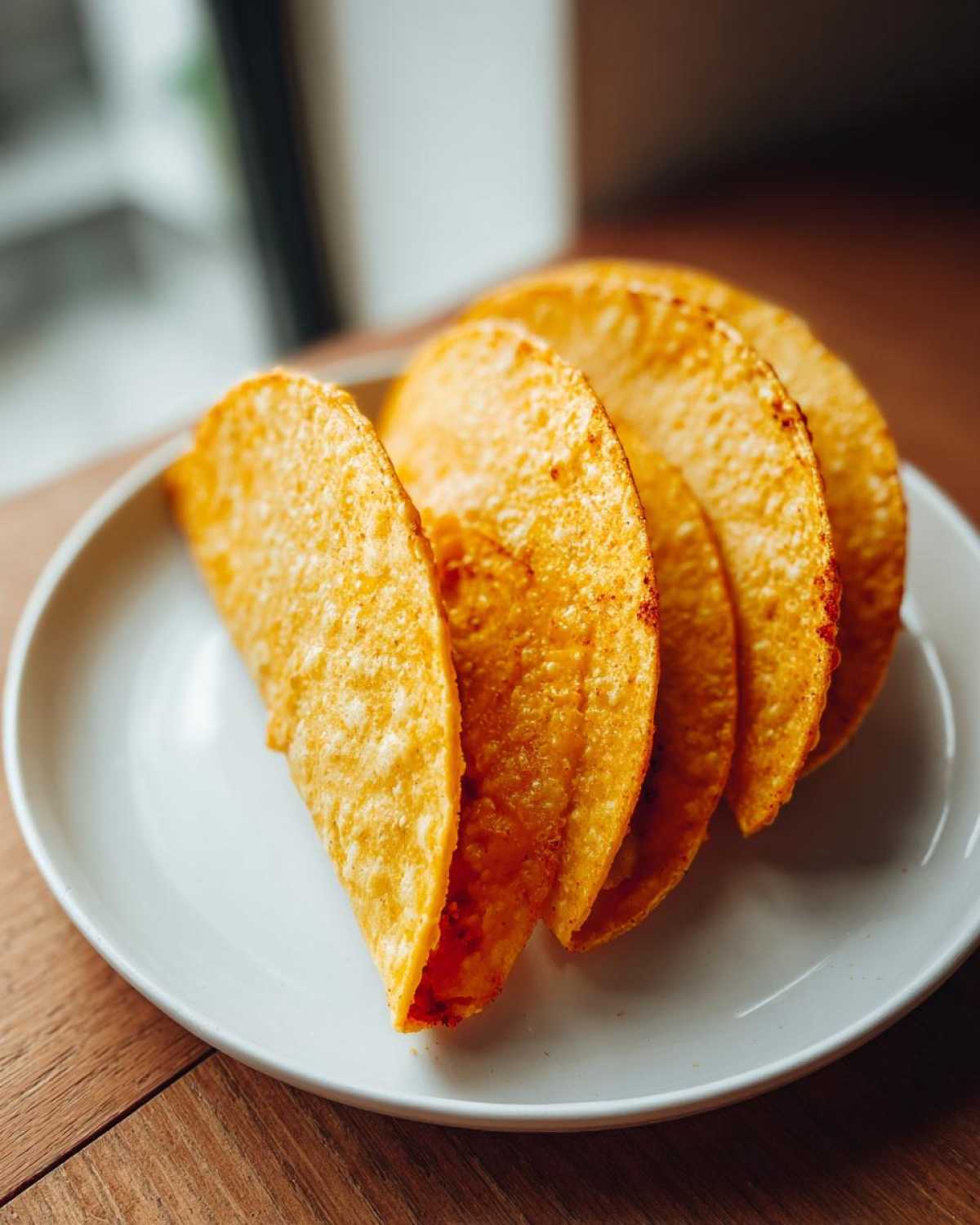 Four golden, crispy Keto Taco Shells with Melted Cheese shells lined up on a white plate, ready to be filled.
