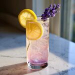 A tall glass of sparkling Lavender Mocktail with Honey, garnished with lemon slices and fresh lavender sprigs.