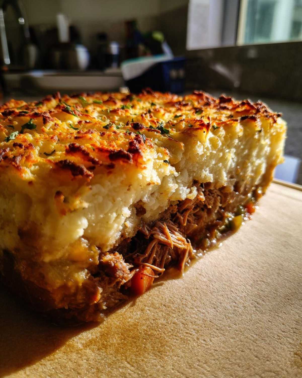 A close-up cross-section of Leftover Lamb Shepherd's Pie, showing shredded lamb filling and a golden, crispy mashed potato topping.