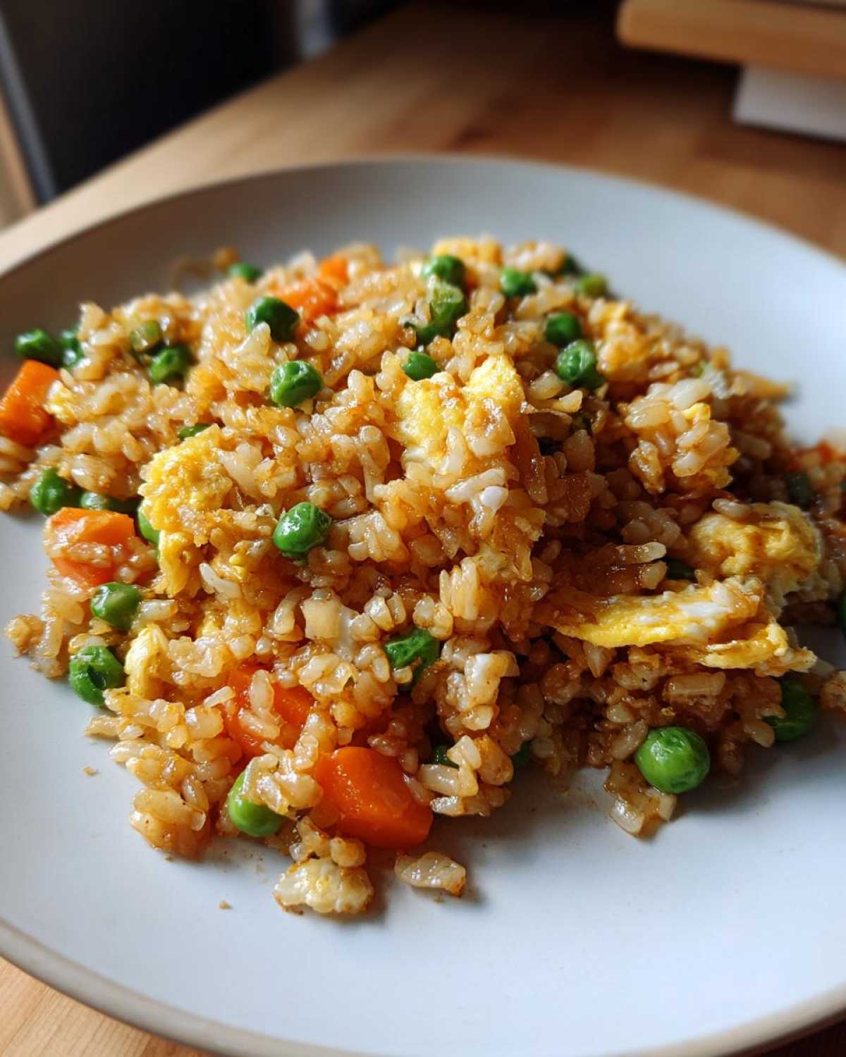 A close-up serving of delicious Leftover Rice Fried Rice, featuring scrambled egg pieces, bright green peas, and diced carrots.