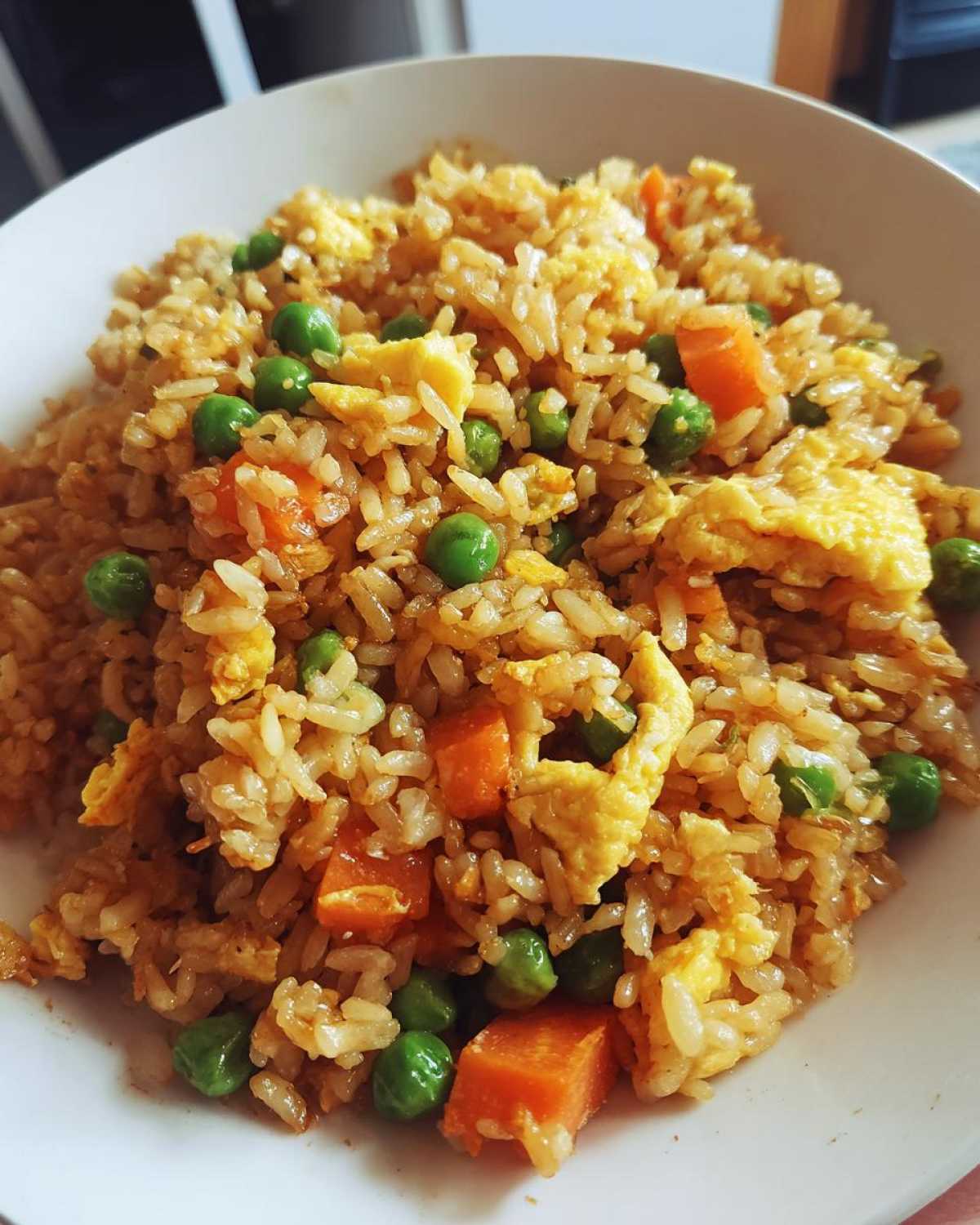 Close-up of a bowl of savory Leftover Rice Fried Rice Recipe mixed with scrambled egg, bright green peas, and diced carrots.