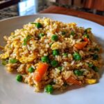 Close-up of a serving of Leftover Rice Fried Rice Recipe, featuring rice, scrambled egg, bright green peas, and diced carrots.