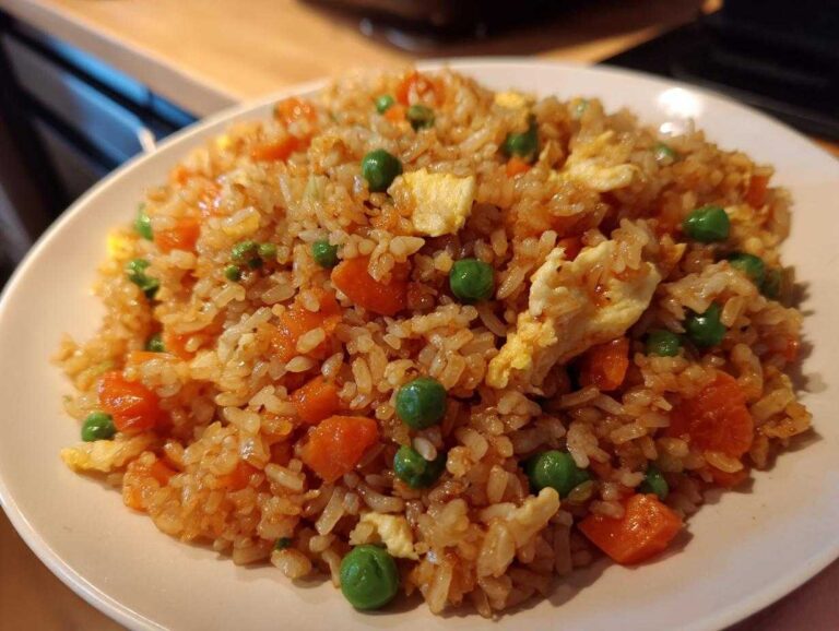 A close-up of a plate filled with colorful Leftover Rice Fried Rice Recipe, featuring rice, scrambled egg, peas, and carrots.