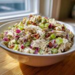 A close-up of a white bowl filled with creamy Leftover Rotisserie Chicken Salad featuring shredded chicken, celery, red onion, and pecans.