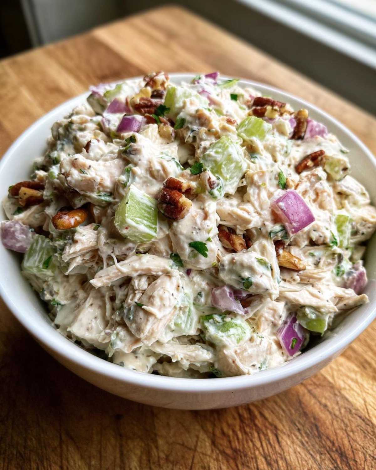 Close-up of a creamy bowl of Leftover Rotisserie Chicken Salad mixed with celery, red onion, and pecans.