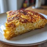 A thick, golden-brown slice of Leftover Spaghetti Frittata Recipe served on a speckled white plate.