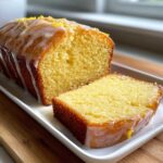 A close-up of a sliced Lemon Olive Oil Pound Cake drizzled with white glaze and topped with lemon zest.