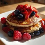 A stack of fluffy Lemon Ricotta Pancakes topped high with fresh strawberries, blueberries, and raspberries.