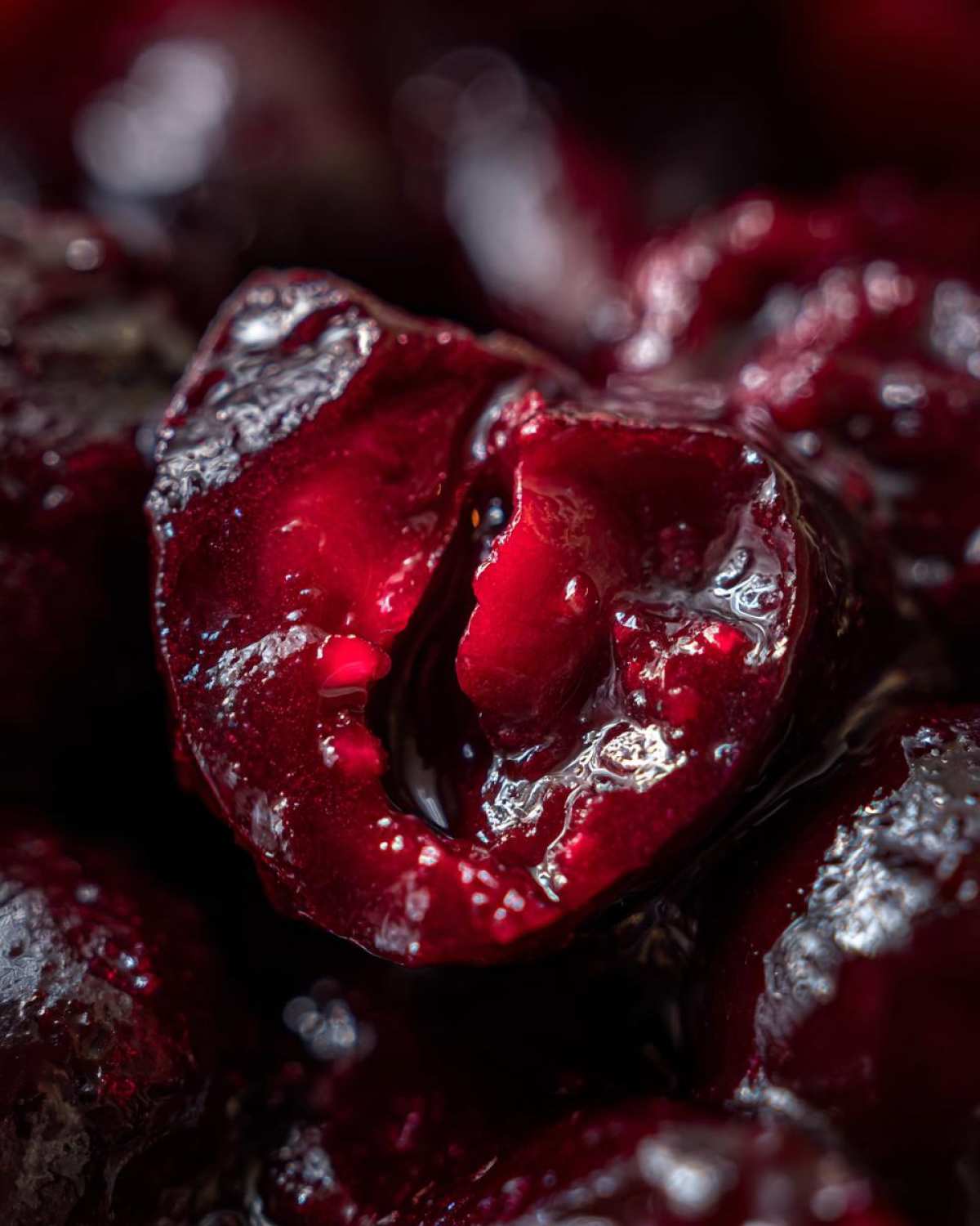 Extreme close-up of a glistening, halved cherry showing the deep red color of the cherry pie filling.