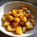 Close-up of shiny, golden Maple Roasted Parsnips Side dish sprinkled with fresh thyme in a white bowl.
