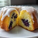 Close-up of a mini blueberry cake, cut in half, showing moist yellow crumb and white glaze, perfect for Cake Picnic Boxed Mini Cakes.