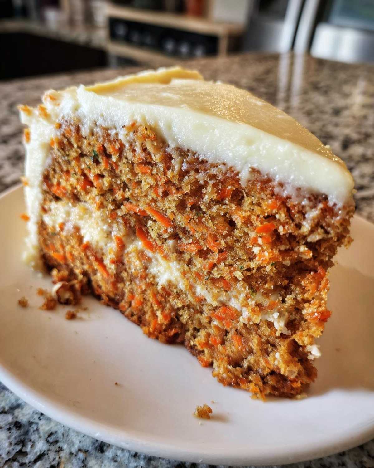 Close-up of a thick slice of moist carrot cake loaded with shredded carrots and topped with rich cream cheese frosting.
