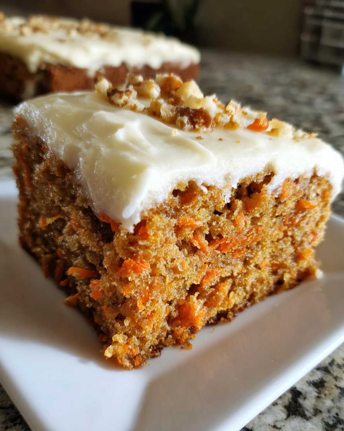 Close-up of a moist slice of carrot cake topped with thick cream cheese frosting and chopped walnuts.