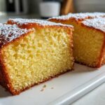 Close-up of a moist, yellow olive oil cake loaf, dusted with powdered sugar, sliced to show the crumb.