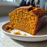 Close-up of a thick slice of super moist pumpkin bread showing its rich orange color and tender crumb texture.