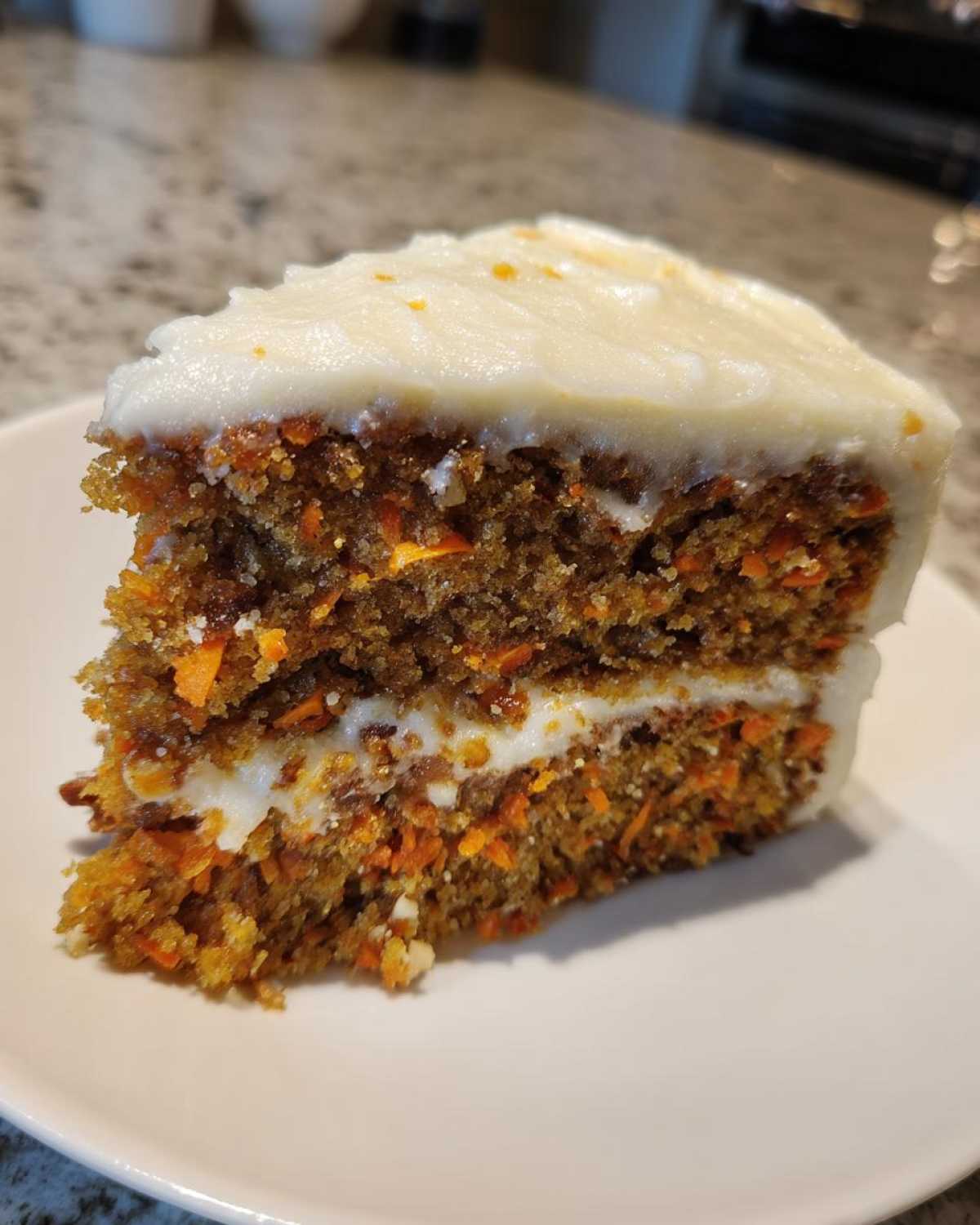 A close-up slice of moist carrot cake featuring two layers filled and topped with thick cream cheese frosting.