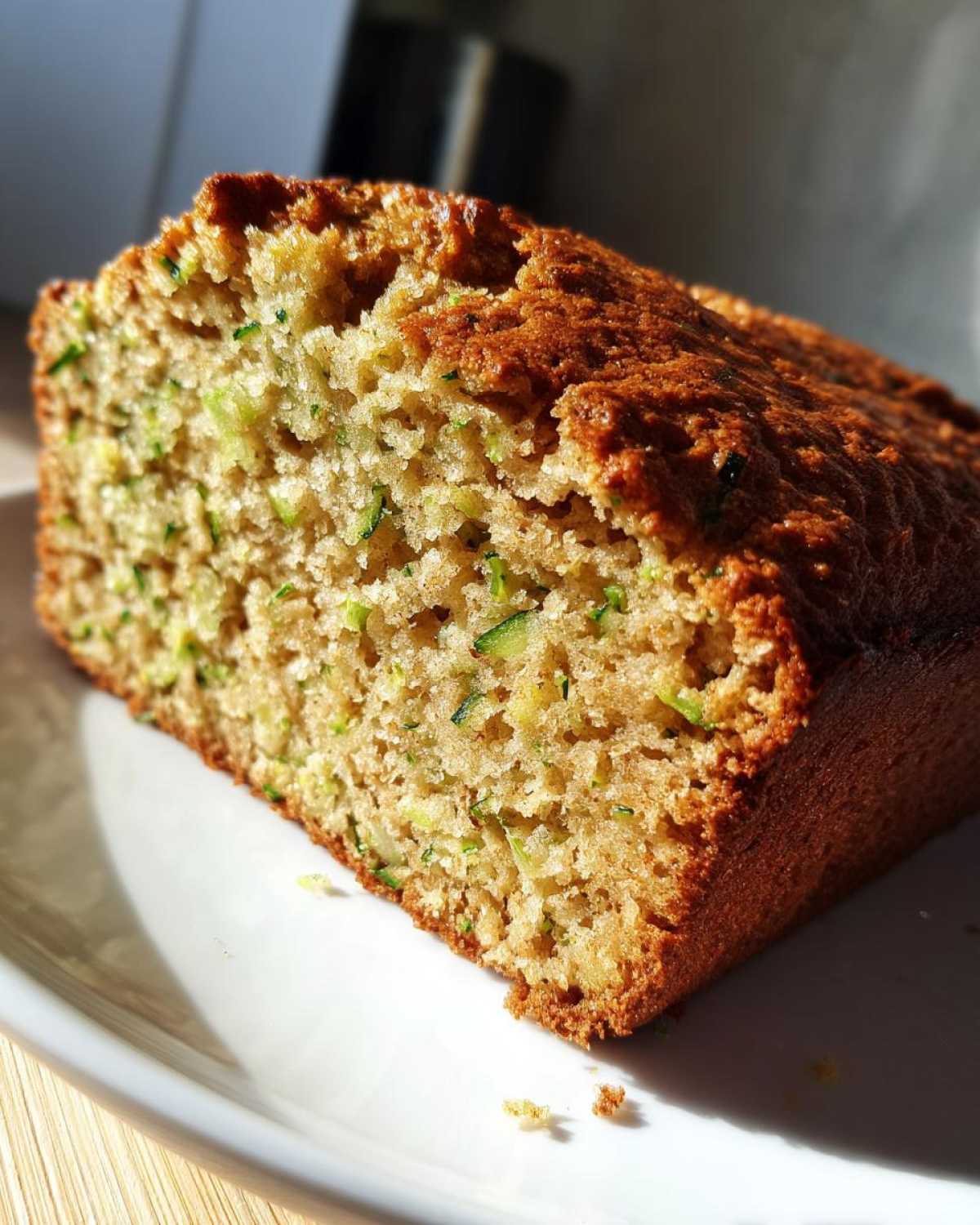 Close-up of a moist slice of zucchini bread recipe showing visible shreds of green zucchini throughout the crumb.