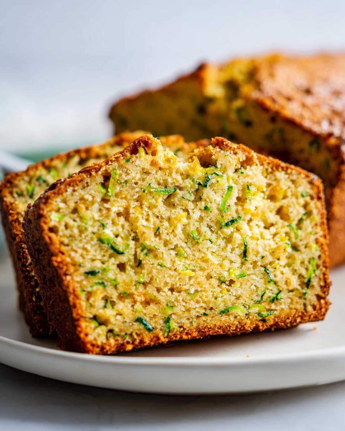 Close-up of moist slices of zucchini bread recipe showing shredded green zucchini throughout the golden crumb.