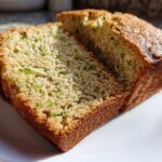 Close-up of three thick slices of golden brown zucchini bread recipe showing moist crumb and flecks of green zucchini.