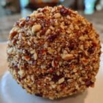 Close-up of a perfectly formed cheese ball recipe coated entirely in finely chopped, toasted pecans.