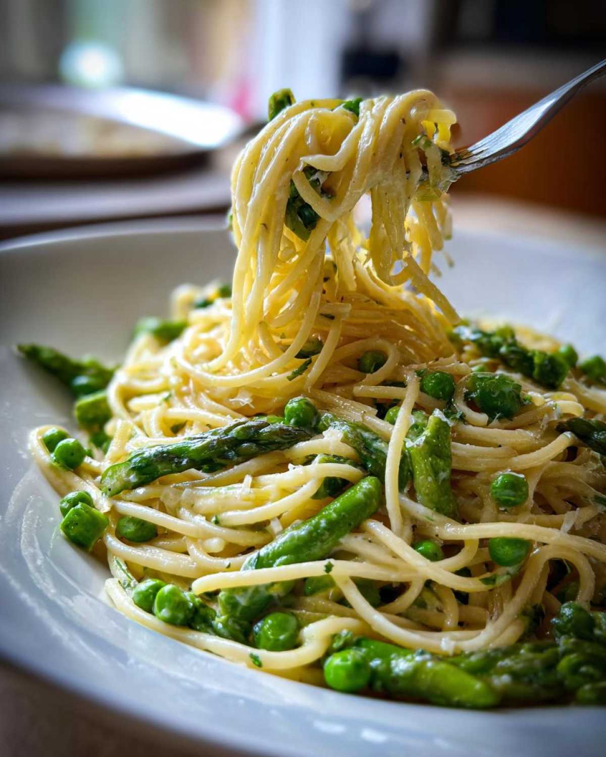 A fork lifting spaghetti noodles coated in sauce, mixed with bright green peas and asparagus tips from a bowl of One Pot Spring Pasta Primavera.