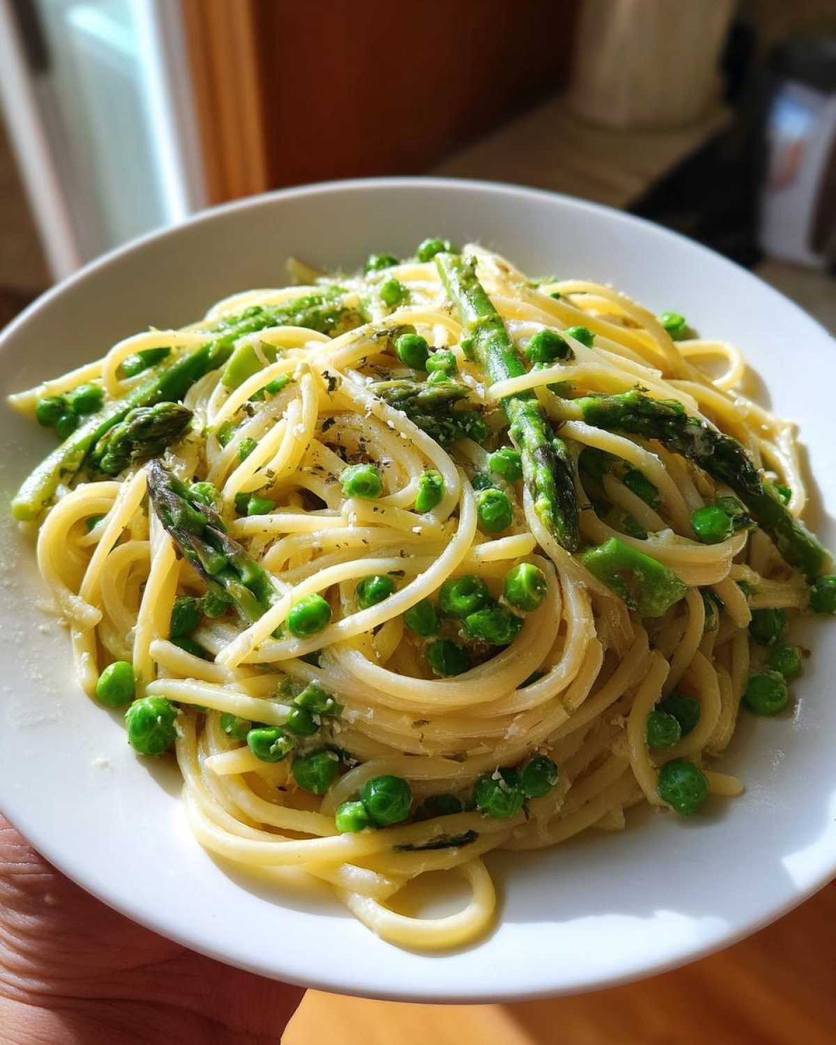 Close-up of a serving of One Pot Spring Pasta Primavera featuring spaghetti, bright green peas, and asparagus tips, sprinkled with cheese.