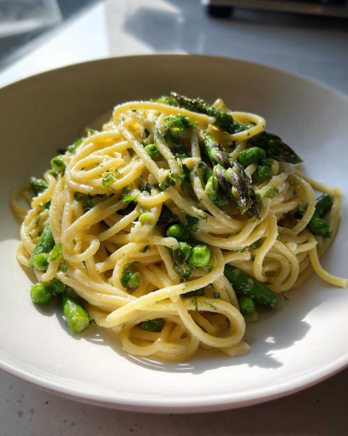 Close-up of a white bowl filled with One Pot Spring Pasta Primavera featuring bright green peas and asparagus tips.