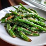 A close-up of vibrant Oven Roasted Green Beans With Garlic Parmesan piled on a white plate.