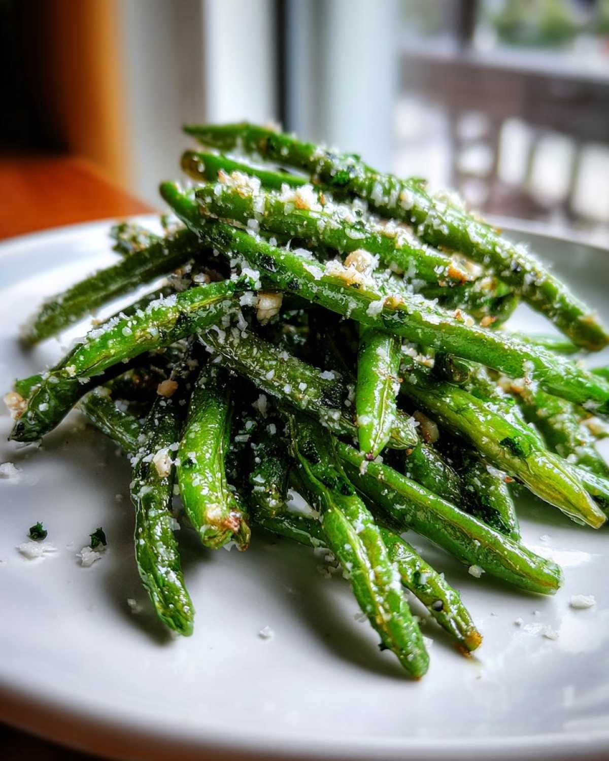 A close-up of bright green Oven Roasted Green Beans With Garlic Parmesan piled high on a white plate.