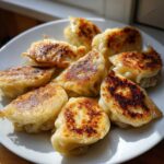 A plate of golden-brown, crispy Pan Fried Cabbage Dumplings arranged attractively under bright sunlight.