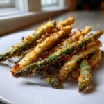 A close-up of freshly cooked, crispy Parmesan Asparagus Fries piled on a white plate.