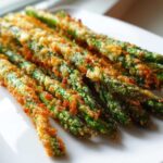 Close-up of several crispy Parmesan Asparagus Fries, golden brown and vibrant green, served on a white plate.