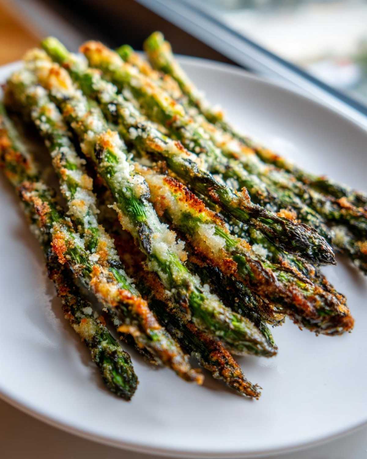 A close-up of crispy, oven-roasted Parmesan Asparagus Fries piled on a white plate.