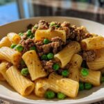 Close-up of a bowl filled with rigatoni pasta, ground lamb, and bright green peas, showcasing the Pea and Lamb Pasta Comfort.