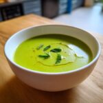 A close-up of bright green Pea and Mint Soup Refreshing, garnished with fresh mint leaves and a drizzle of olive oil.