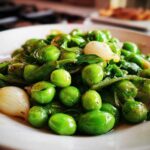 Close-up of bright green Petits Pois à la Française mixed with small pearl onions and herbs on a white dish.