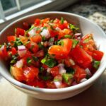 Close-up of fresh, chunky Pico De Gallo Recipe Zesty ingredients including diced tomatoes, red onion, and cilantro in a white bowl.