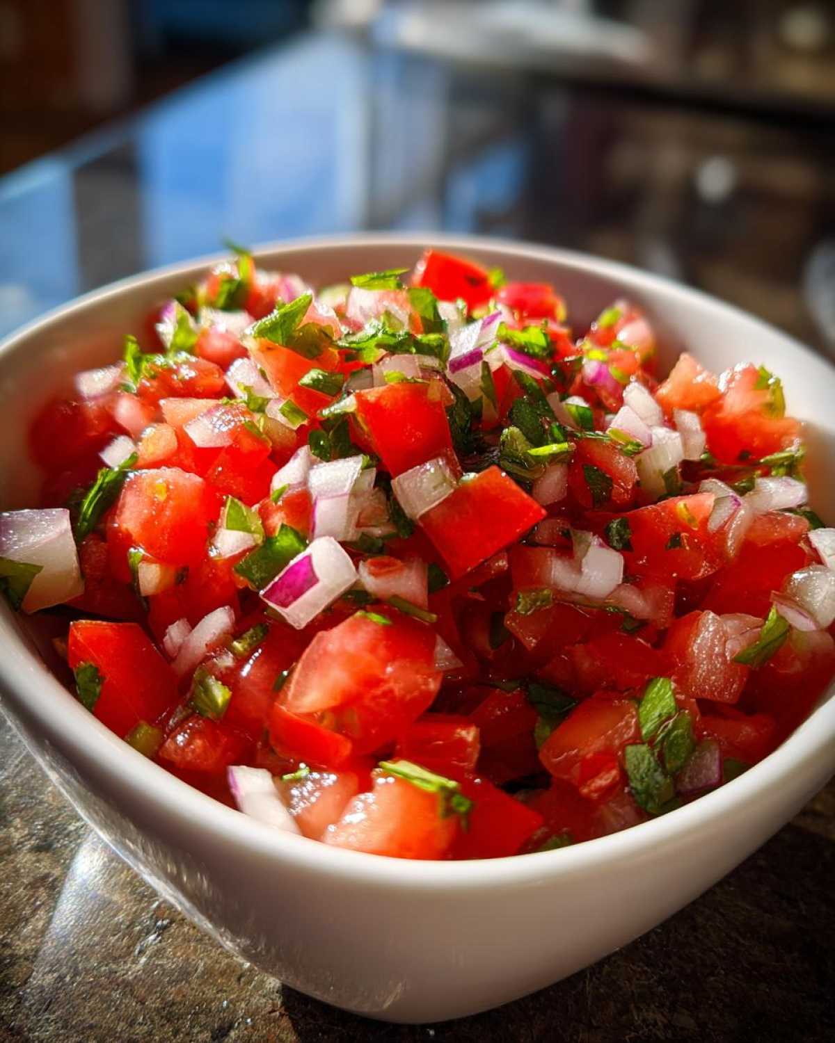 Close-up of fresh Pico De Gallo Recipe Zesty ingredients: diced tomatoes, red onion, and cilantro in a white bowl.