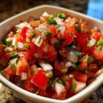 Close-up of vibrant, freshly chopped tomatoes, onions, and cilantro in a white bowl for a Pico De Gallo Recipe Zesty.