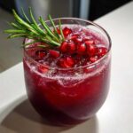Close-up of a chilled Pomegranate Spritz Cocktail topped with fresh pomegranate seeds and a sprig of rosemary.