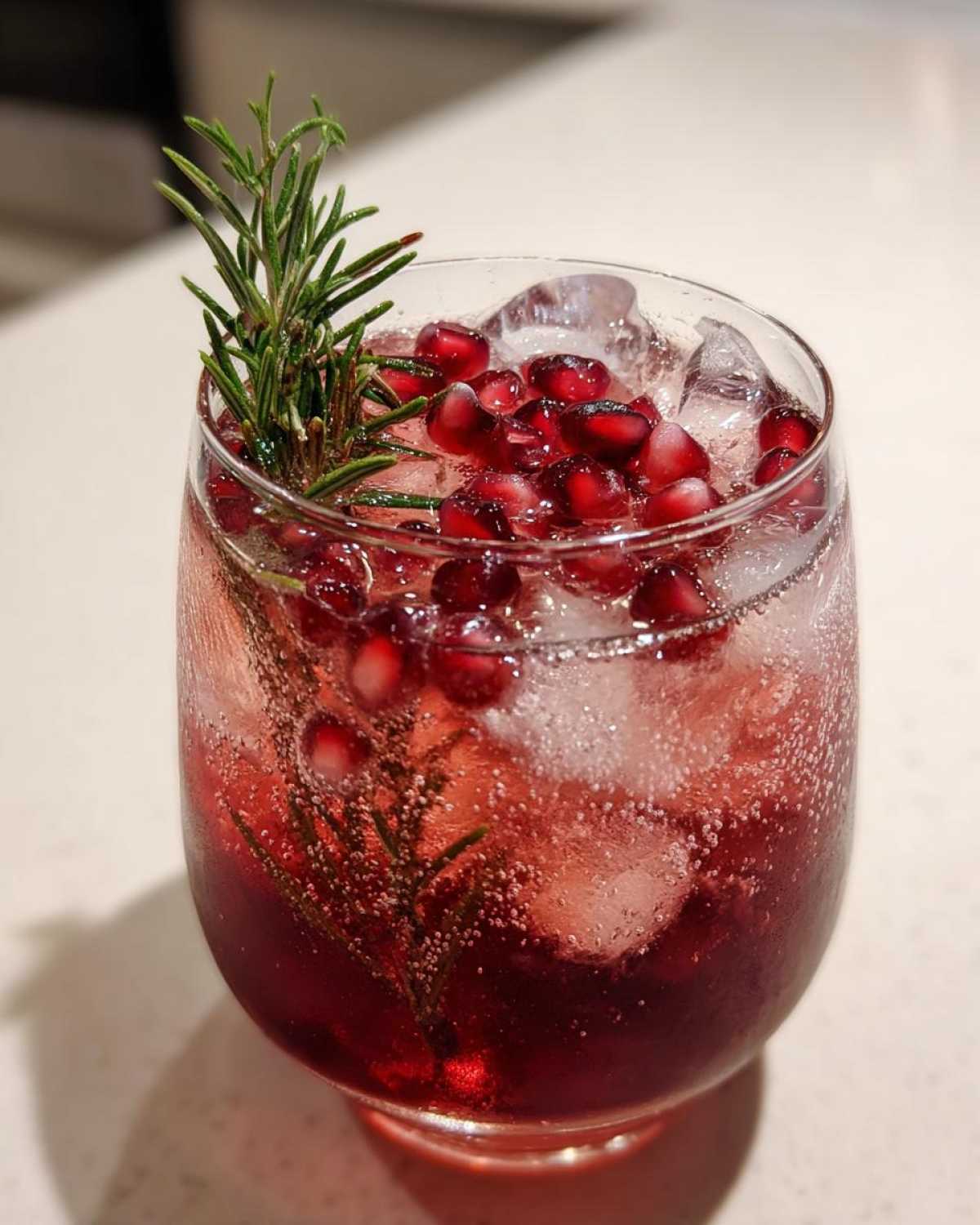 Close-up of a fizzy Pomegranate Spritz Cocktail garnished with fresh pomegranate seeds and a sprig of rosemary.