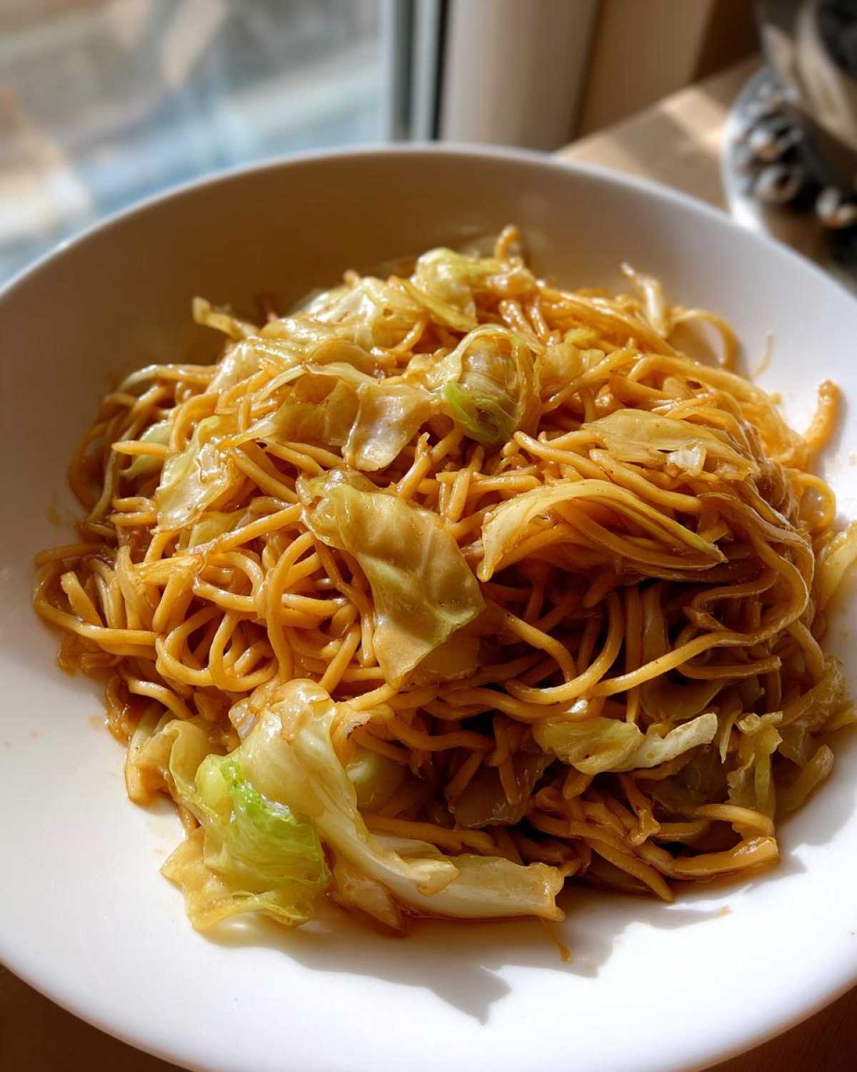 A close-up of a serving of Cabbage Noodle Stir Fry 10 Mins in a white bowl, glistening with sauce.