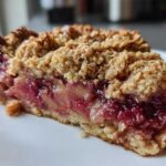 Close-up of a rich slice of Rhubarb Crumble with Vanilla Bean, showing thick oat topping and bright pink fruit filling.